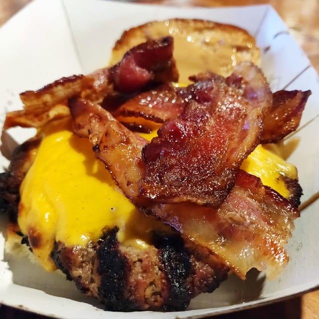 Juicy burger topped with crispy bacon and melted cheddar cheese, showcasing a deliciously messy presentation, featured in a review of Portland's Burger Week.